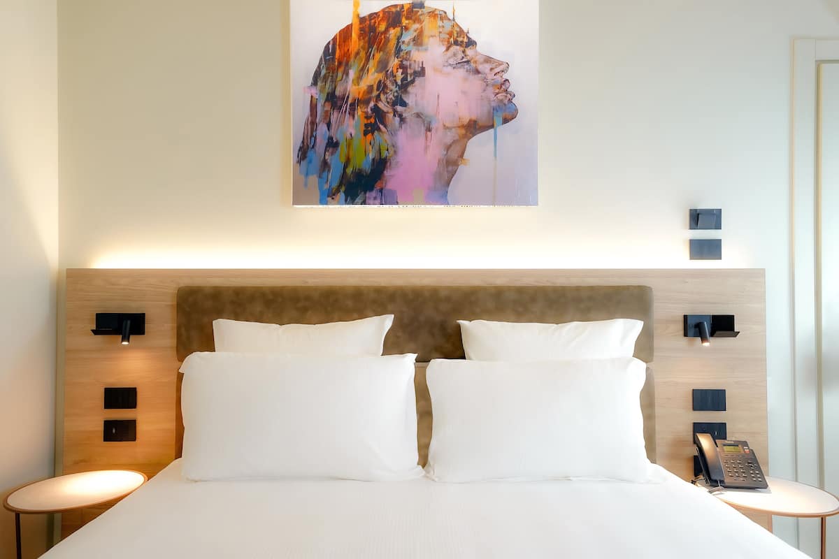 A hotel room with a large bed, two bedside tables, a headboard, and a wall-mounted artwork.