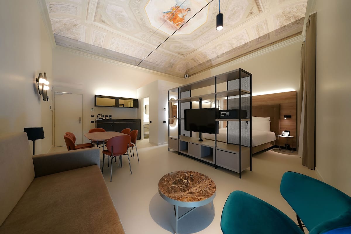 A modern hotel room with a dining area, a TV, a sofa, and a ceiling with intricate designs.