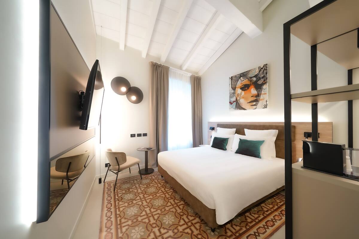 A modern hotel room with a large bed, a flat-screen TV, a small desk, and a chair.