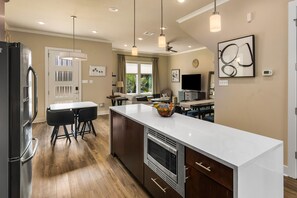 Une cuisine moderne dotée d’un îlot central, de meubles en bois foncé, d’appareils électroménagers en acier inoxydable et de luminaires suspendus.
