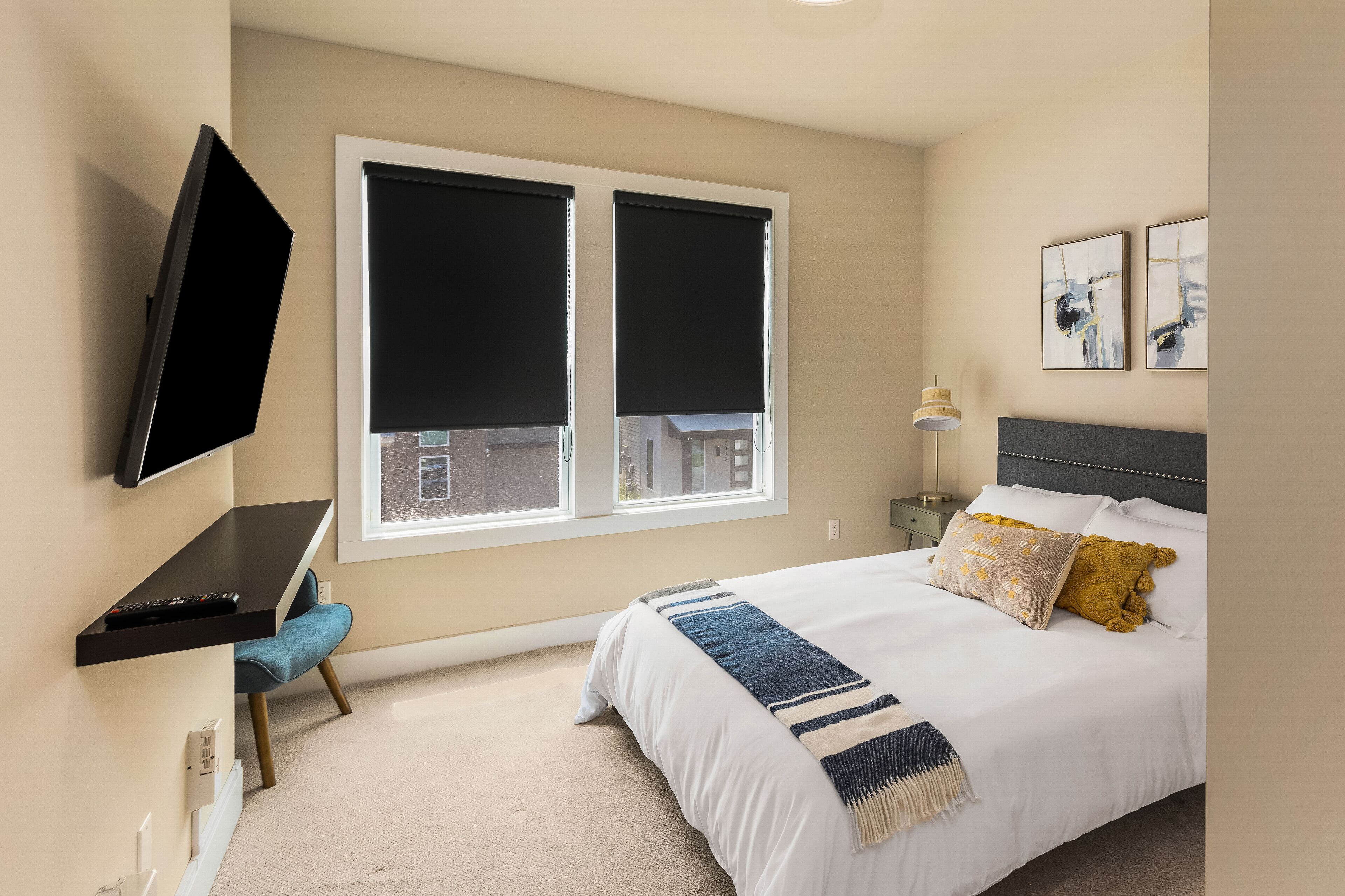Un dormitorio con cama, escritorio, televisor y dos ventanas con persianas.