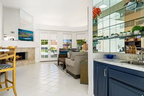A modern kitchen with a large island, a dining area with a fireplace, and a living room with a sofa and chairs.