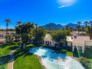 A resort with a swimming pool, palm trees, and mountains in the background.
