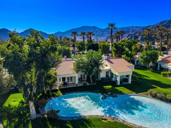 A residential area with a swimming pool surrounded by lush greenery and palm trees.