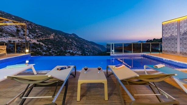 An outdoor pool area with lounge chairs and a table, overlooking a mountainous landscape.