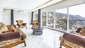 A spacious room with a large window offering a mountain view, two armchairs, a round coffee table, and a modern ceiling design.