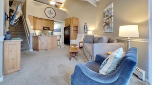 A spacious living area with a kitchen, a blue armchair, a sofa, and a dining table. - 211 Pointes North | Dog Friendly | Downtown Charlevoix | Indoor/Outdoor Pool (Charlevoix)