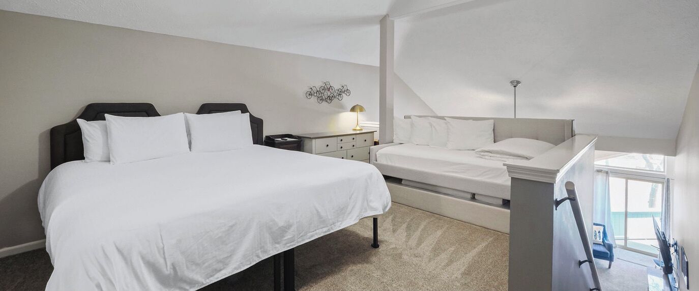 A bedroom with a large bed, a bedside table with a lamp, and a window with a view.
