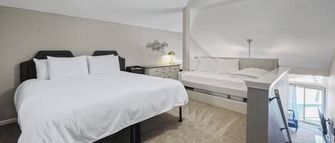 A bedroom with a large bed, a bedside table with a lamp, and a window with a view.