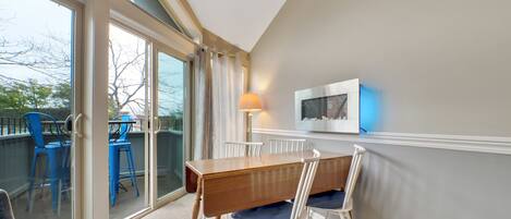 A dining area with a wooden table and white chairs, a glass door leading outside, and a wall-mounted TV.