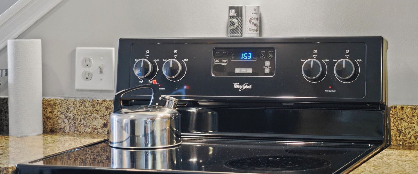 A Whirlpool stove with digital controls, a stainless steel kettle, and granite countertops.