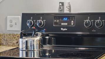 A Whirlpool stove with digital controls, a stainless steel kettle, and granite countertops.