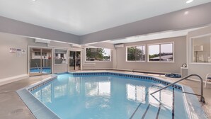 A swimming pool with a blue tiled edge, a glass door entrance, and a view of the outside through large windows. - 211 Pointes North | Dog Friendly | Downtown Charlevoix | Indoor/Outdoor Pool (Charlevoix)