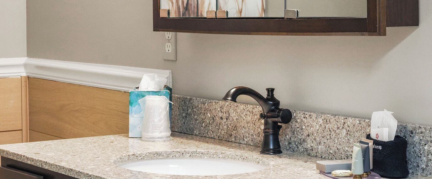 A bathroom with a granite countertop, a sink, a faucet, and toiletries.