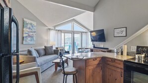A modern kitchen with a large island, a dining area with a sofa and chairs, and a living room with a large window and artwork. - 211 Pointes North | Dog Friendly | Downtown Charlevoix | Indoor/Outdoor Pool (Charlevoix)