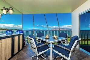 A covered outdoor seating area with a table and chairs, a bar with stools, and a view of the ocean. - Royal Mauian #210 Ocean View, Full A/C, Great Location, Close to beaches! (Kihei)