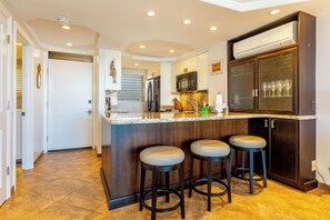 A modern kitchen with a central island, bar stools, a microwave, and a refrigerator. - Royal Mauian #210 Ocean View, Full A/C, Great Location, Close to beaches! (Kihei)