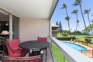 A balcony with a round table and chairs, a view of a swimming pool, and palm trees.