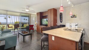 A modern kitchen with a large island, wooden cabinets, and a built-in TV. - Leinaala Oceanfront #203 Panoramic Ocean View, Renovated, A/C, Great Rates! (Kihei)