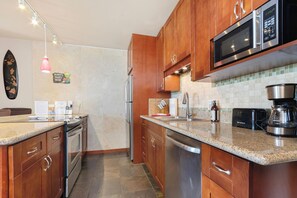 A modern kitchen with wooden cabinets, stainless steel appliances, a granite countertop, and a backsplash with small tiles.