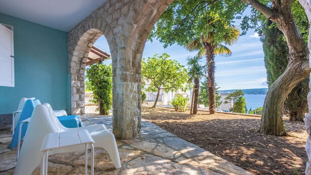 A stone patio with white plastic chairs, a stone wall, and a view of the sea.