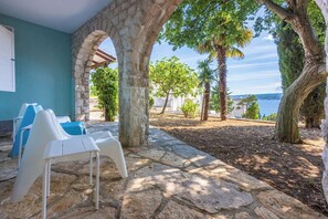 Une terrasse en pierre avec des chaises en plastique blanches, un mur de pierre et une vue sur la mer.