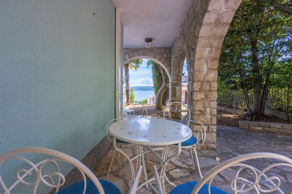 A stone archway leading to a patio with a table and chairs, overlooking a body of water.