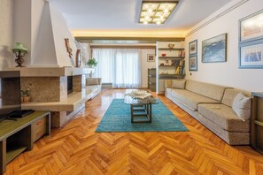 A living room with a herringbone floor, a sofa, a coffee table, a fireplace, and a bookshelf.