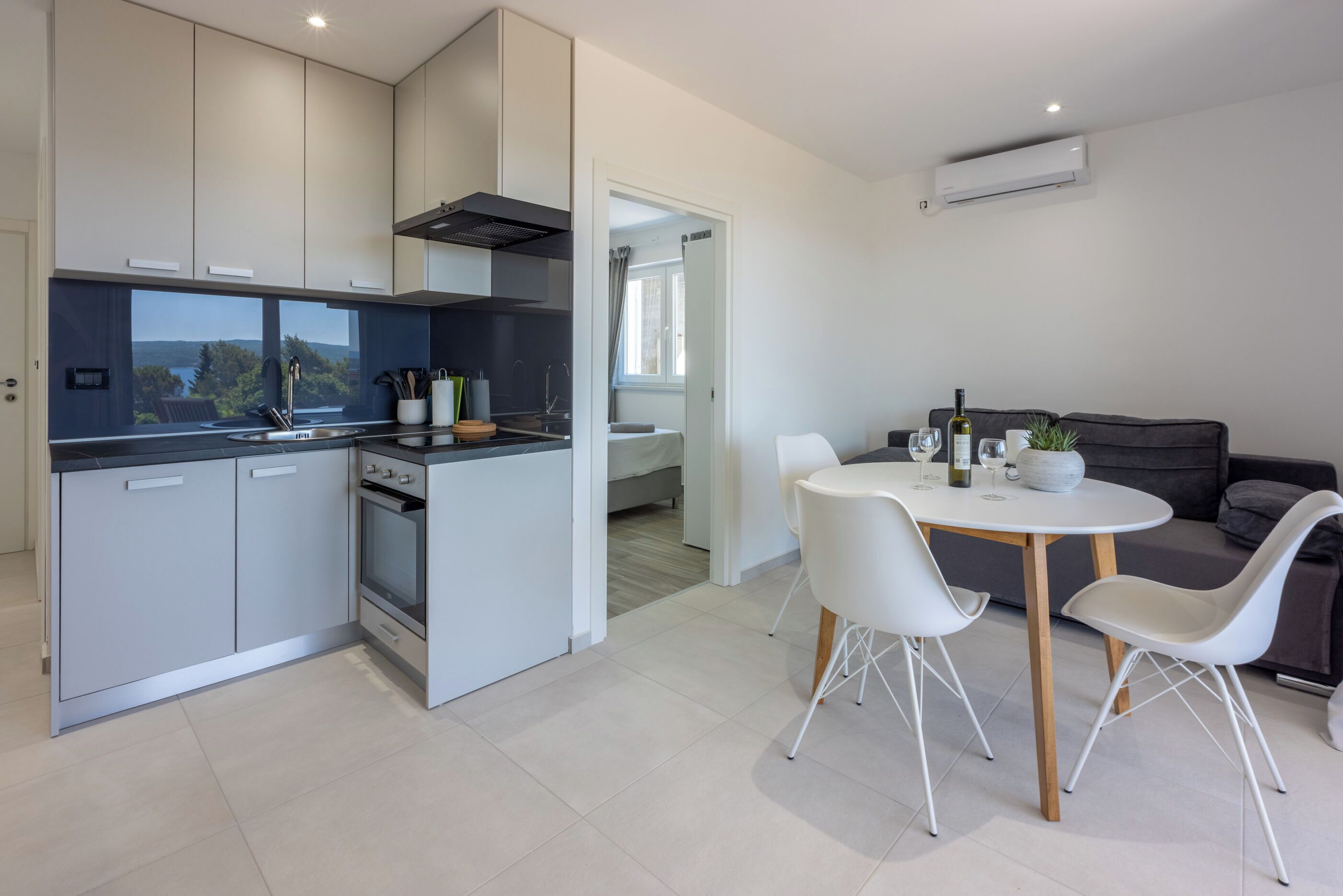 A modern kitchen with grey cabinets, a built-in oven, and a dining area with a white table and chairs.