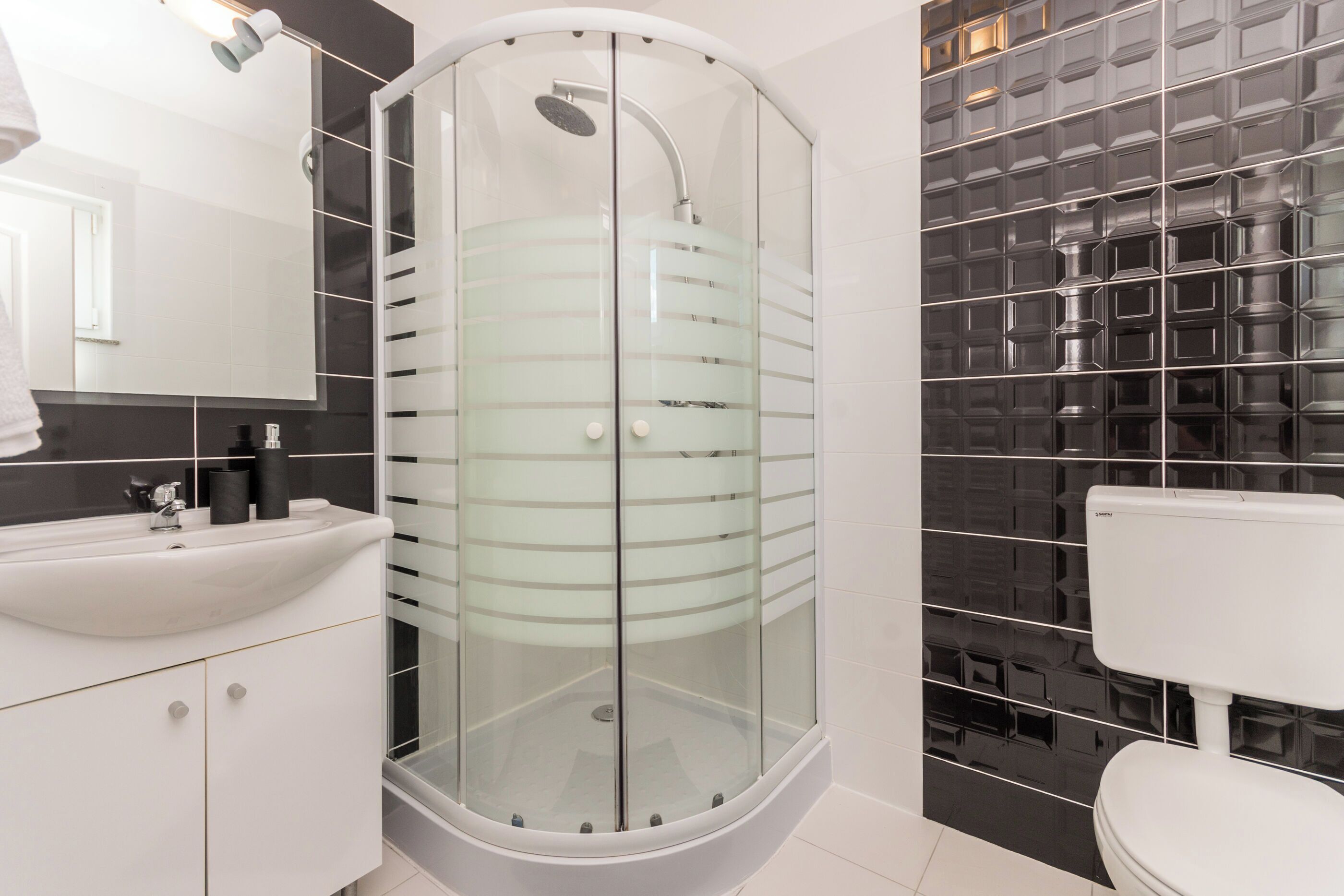 A modern bathroom with a glass-enclosed shower, a white sink, and a toilet.