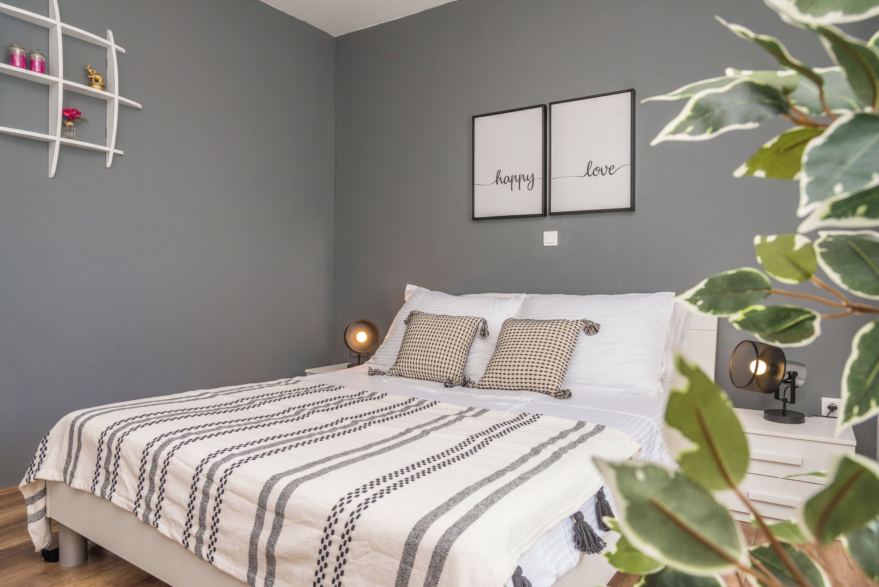 Ein Schlafzimmer mit einem Bett, Nachttischlampen, einer Ablage mit Dekoration und zwei gerahmten Bildern an der Wand.