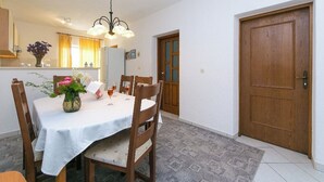 Ein Essbereich mit einem Tisch für vier Personen, Holzsesseln, einer Chandelierleuchtre und einer Holztür.