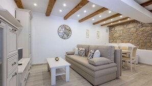 A cozy living room with a beige sofa, a small white table, and a stone wall. - Villa Green Point (Grizane)