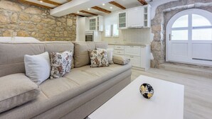 A modern living room with a stone wall, wooden beams, a beige sofa, and a white coffee table. - Villa Green Point (Grizane)