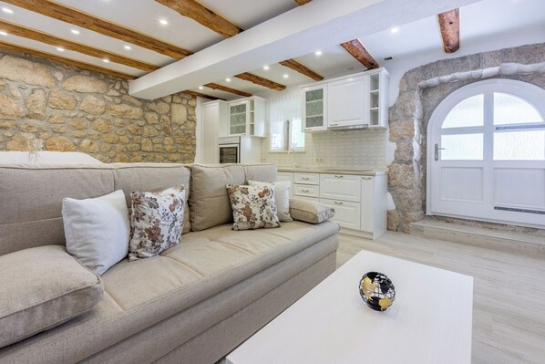 Ein modernes Wohnzimmer mit Steinwand, Holzbalken, einem beigefarbenen Sofa und einem weißen Couchtisch.