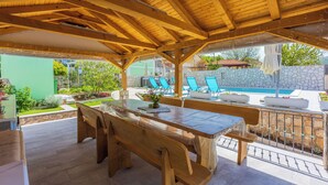 An outdoor patio with a wooden table and benches, a pool, and lounge chairs. - Villa Green Point (Grizane)