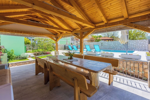 Un patio al aire libre con mesa y bancos de madera, una piscina y sillas de descanso.