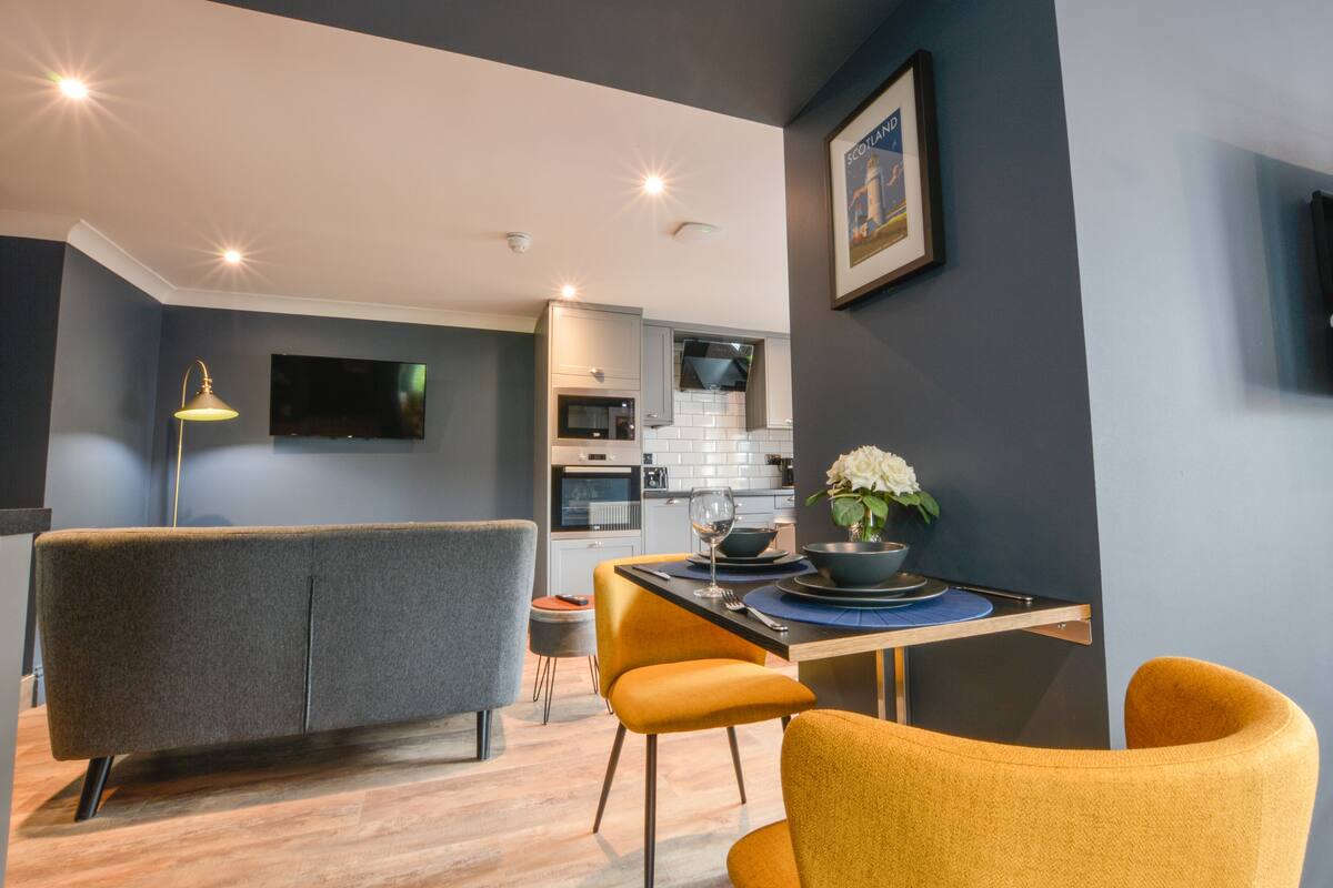 A modern kitchen with grey cabinets, a microwave, and a sink. There is a dining area with a table, chairs, and a vase with flowers.