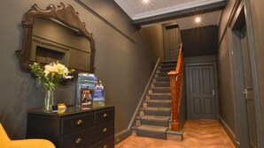 A hallway with a staircase, a dresser with a vase of flowers, and a mirror on the wall.