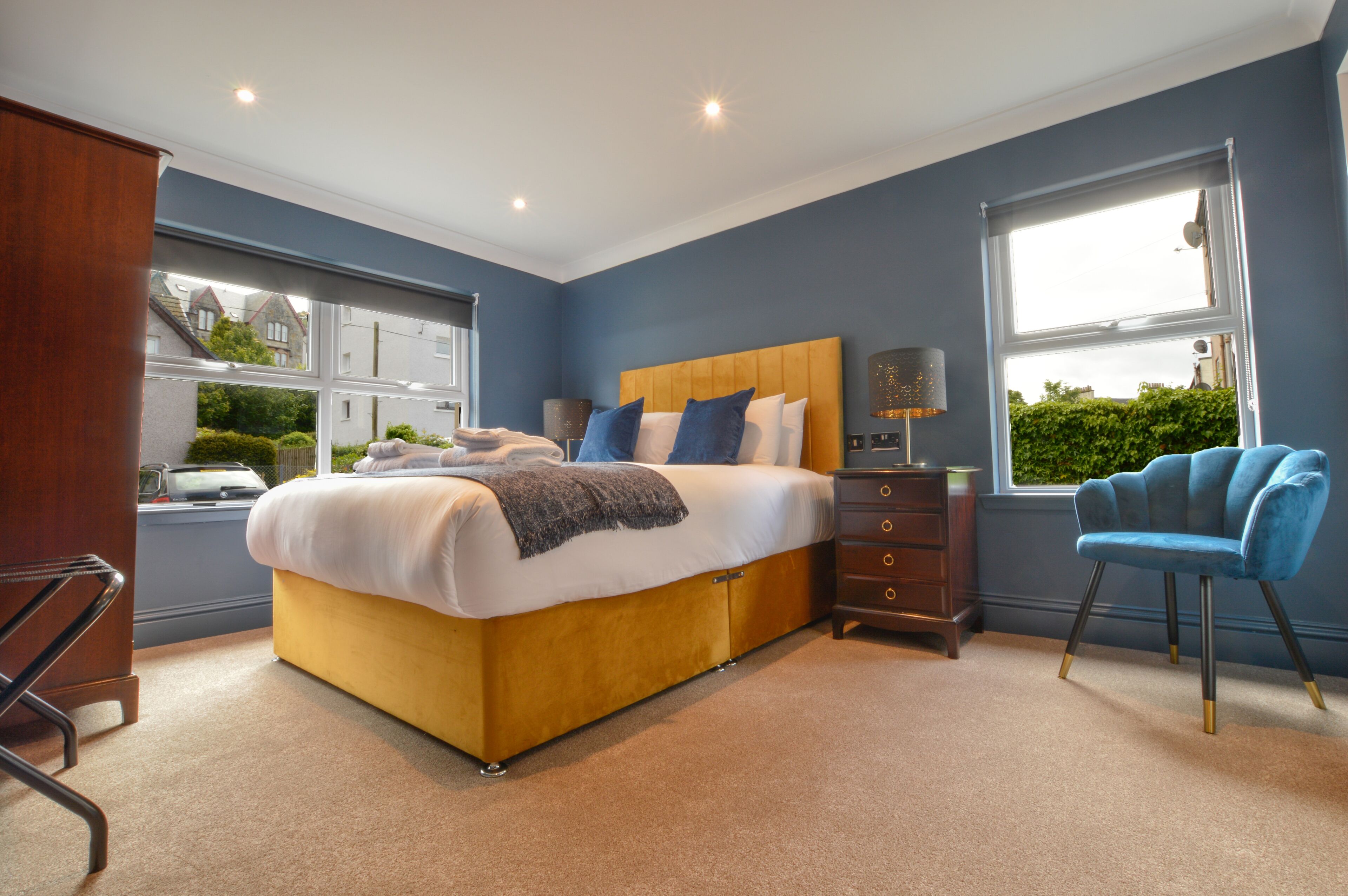 A bedroom with a bed, dresser, chair, and windows.
