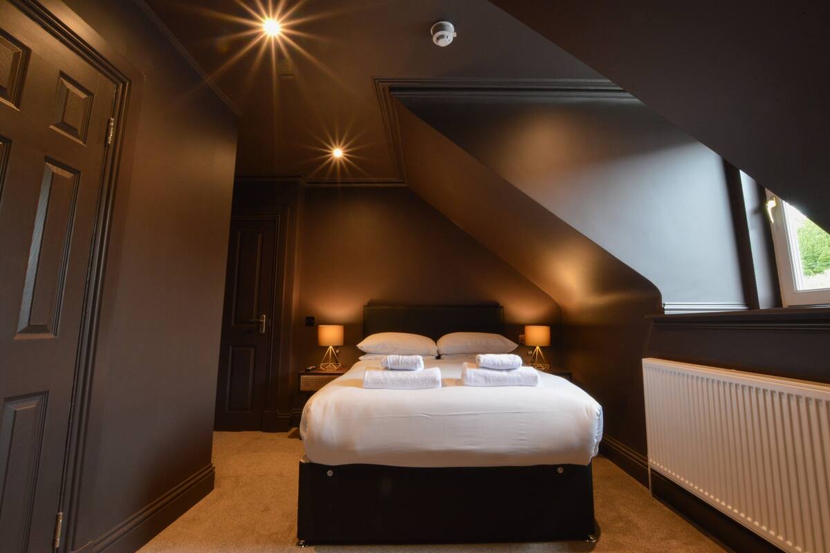 A bedroom with a large bed, two bedside tables with lamps, a ceiling light, and a window.