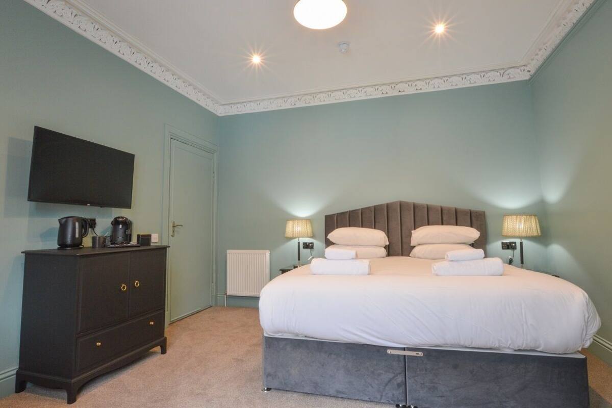 A bedroom with a bed, a dresser, a television, and lamps.