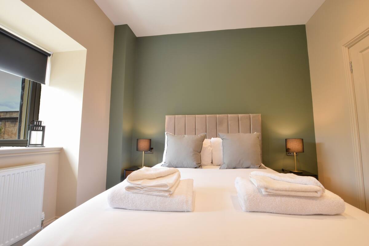 A neatly made bed with two folded towels, a headboard, and two bedside lamps.