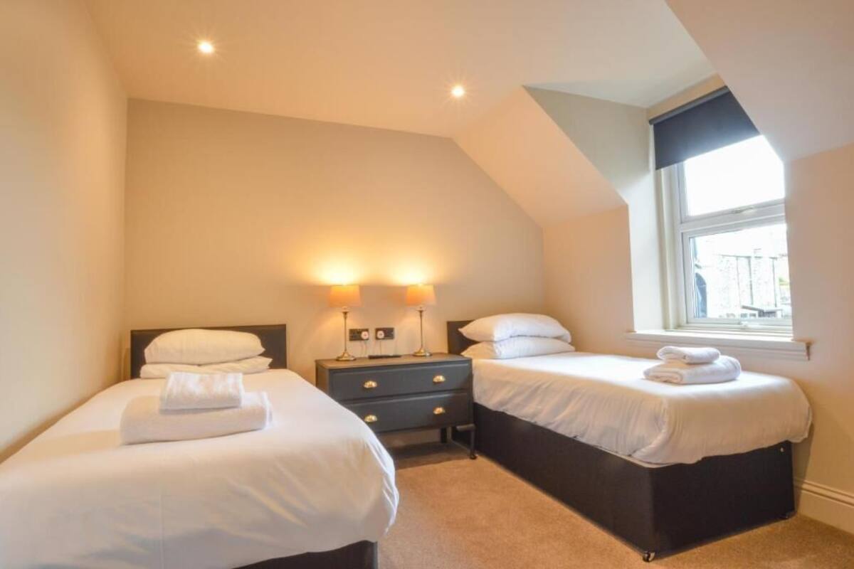 A bedroom with two beds, a nightstand with lamps, and a window with a view.