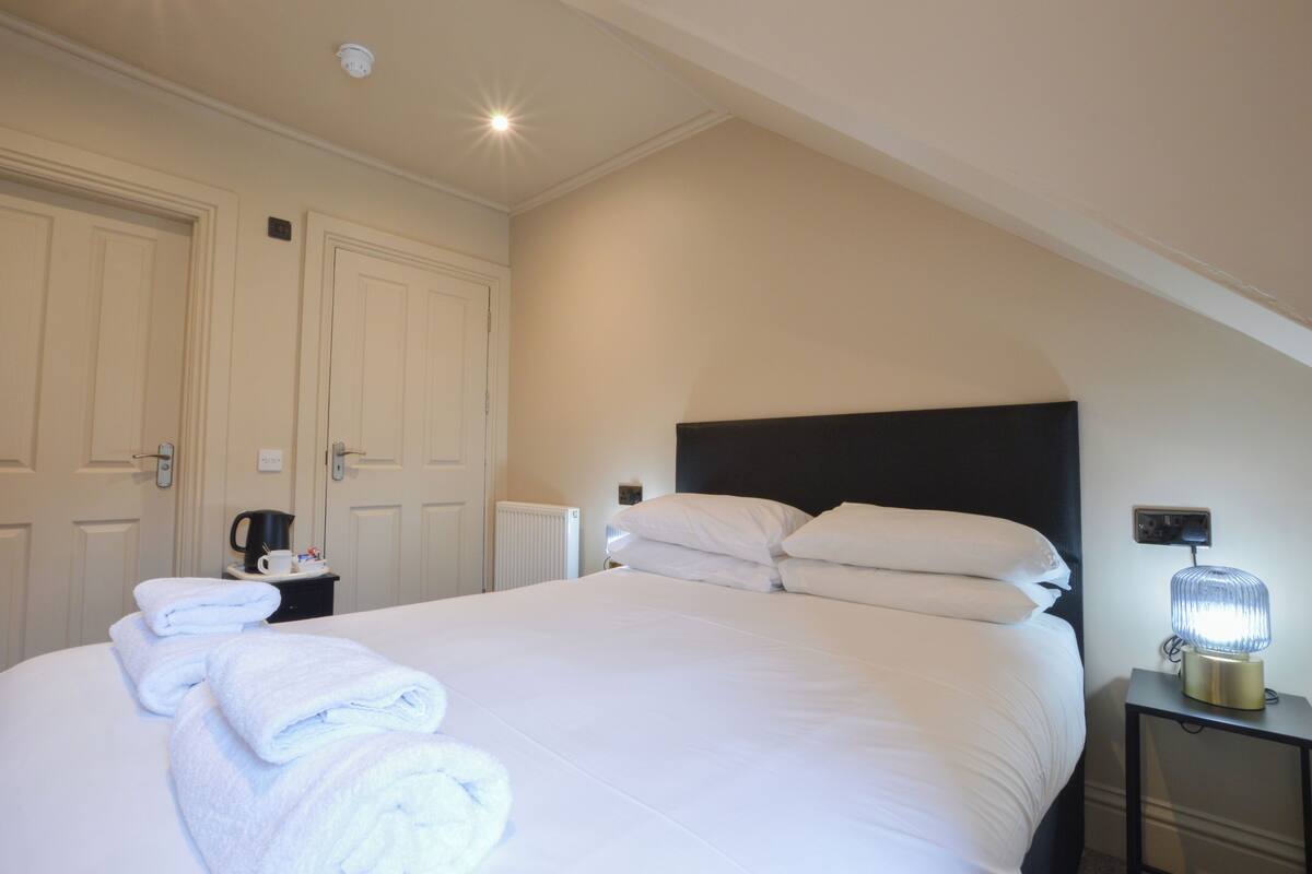 A neatly made bed with white linens, a bedside table with a lamp, and a radiator.