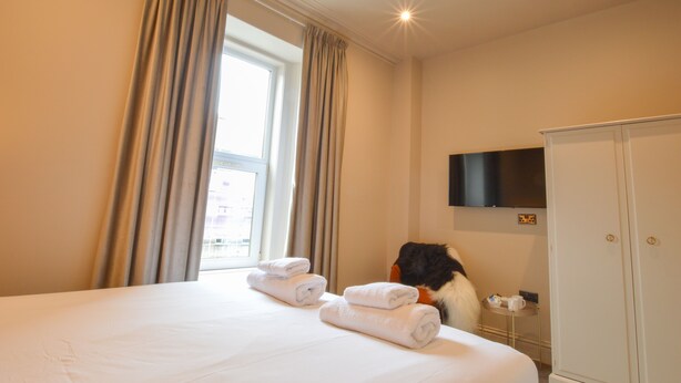 A hotel room with a bed, towels, a television mounted on the wall, and a wardrobe.