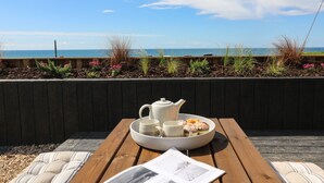 A wooden table with a teapot, cups, and pastries on a deck overlooking the sea. - Sandpiper Chalet (Bridport)