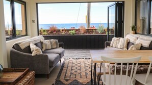A cozy living area with a grey sofa, a wooden coffee table, and a view of the sea through large windows. - Sandpiper Chalet (Bridport)