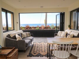 Una sala de estar acogedora con un sofá gris, una mesa de centro de madera y vistas al mar a través de amplios ventanales.