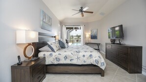 Une chambre à coucher comprenant un lit, des tables de chevet, un ventilateur de plafond, une télévision et une vue sur l’extérieur.